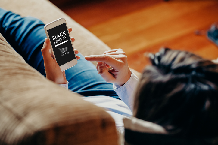 Woman using a mobile phone to buy at Black Friday special offers at home.