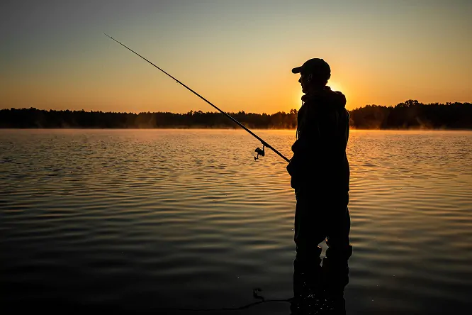 Male fisherman at dawn on the lake catches a fishing rod. Fishing hobby vacation concept. Copy space.