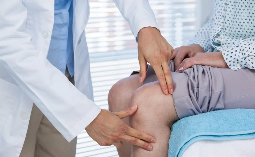 Mid section of doctor examining patient knee in clinic