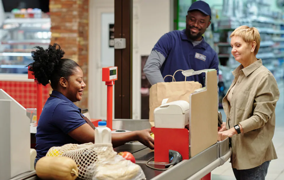 Happy young female cashier scanning food products chosen by customer