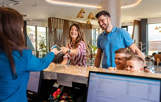 Smiling family of four in the hotel lobby check in at the recept